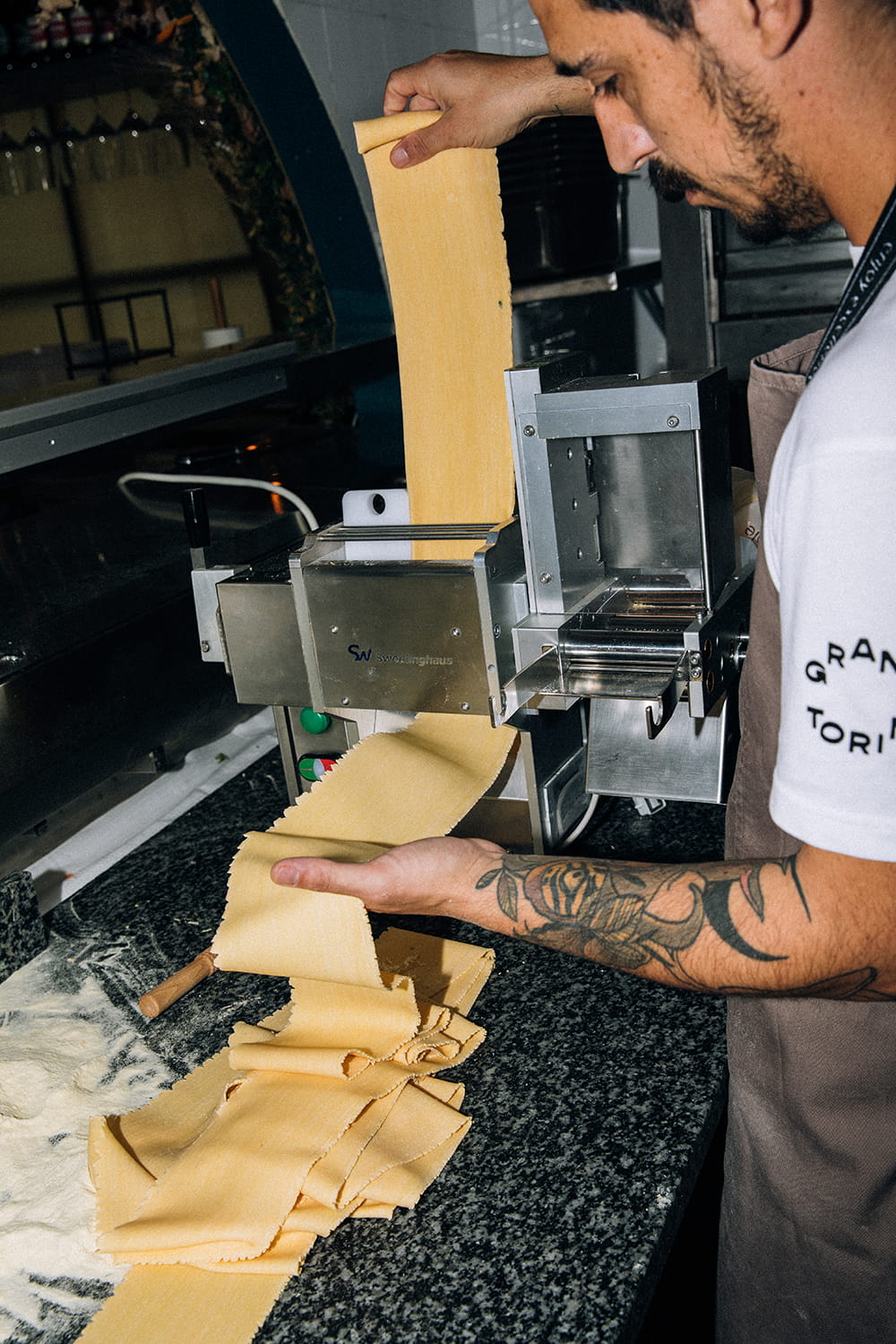 Cocinero preparando pasta fresca en una máquina de pasta dentro de una cocina profesional.