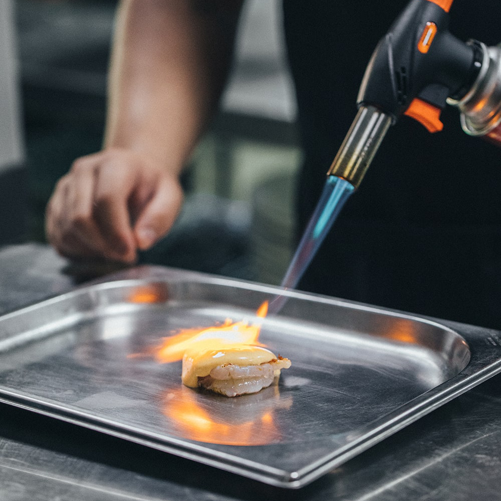 Cocinero flambeando un plato con soplete en una cocina profesional.