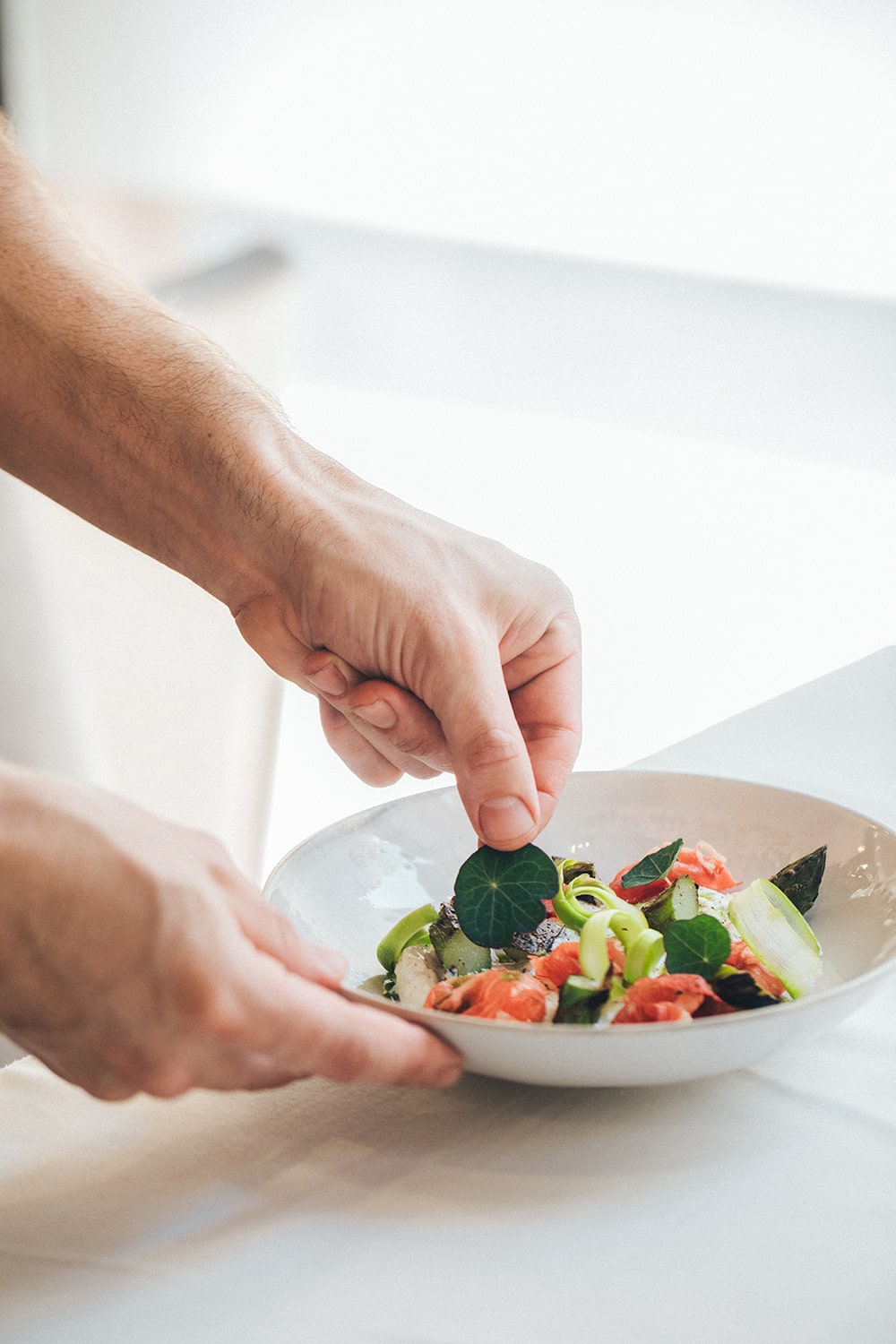 Manos emplatando un plato junto a una entrada de luz natural en un restaurante.