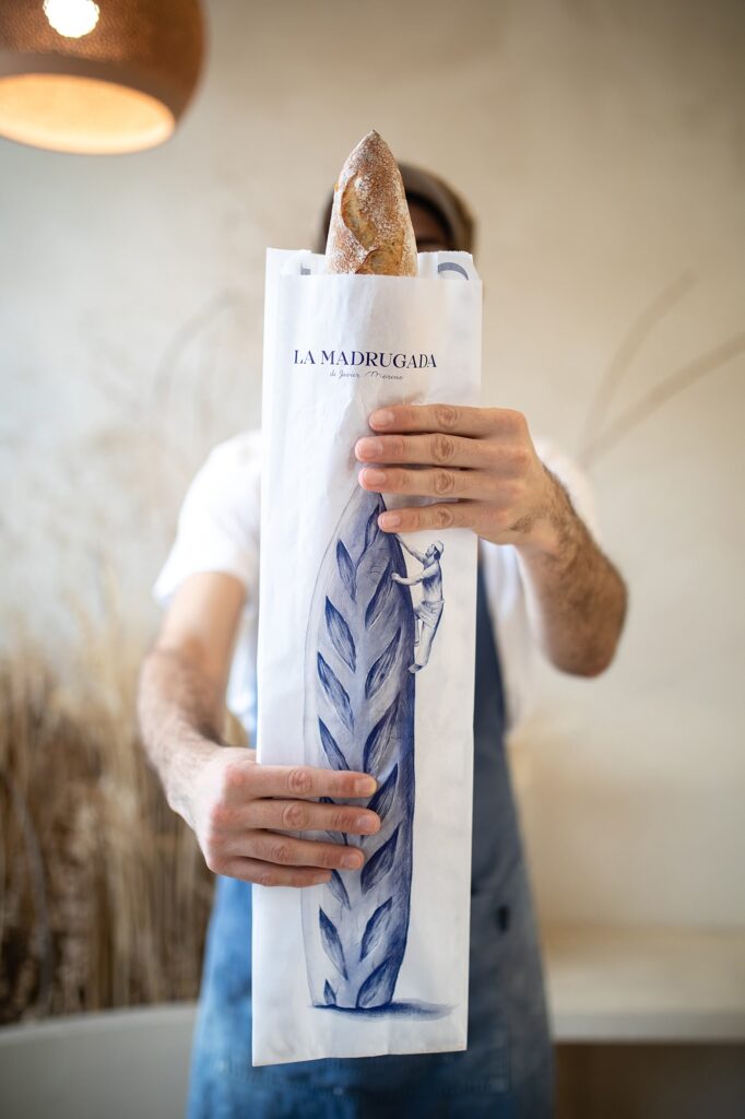 Panadero sosteniendo una barra de pan en una bolsa de La Madrugada dentro de una panadería.